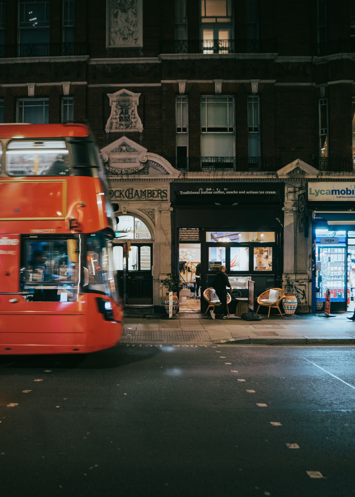 A red double-decker bus on a London street at night