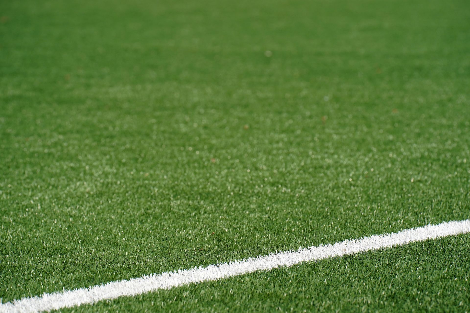 Close-up view of a green artificial soccer field with a white boundary line and space for text.