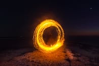在夜晚宁静的海滩上，一名火舞者用迷人的长曝光镜头创造出炽热的圆圈