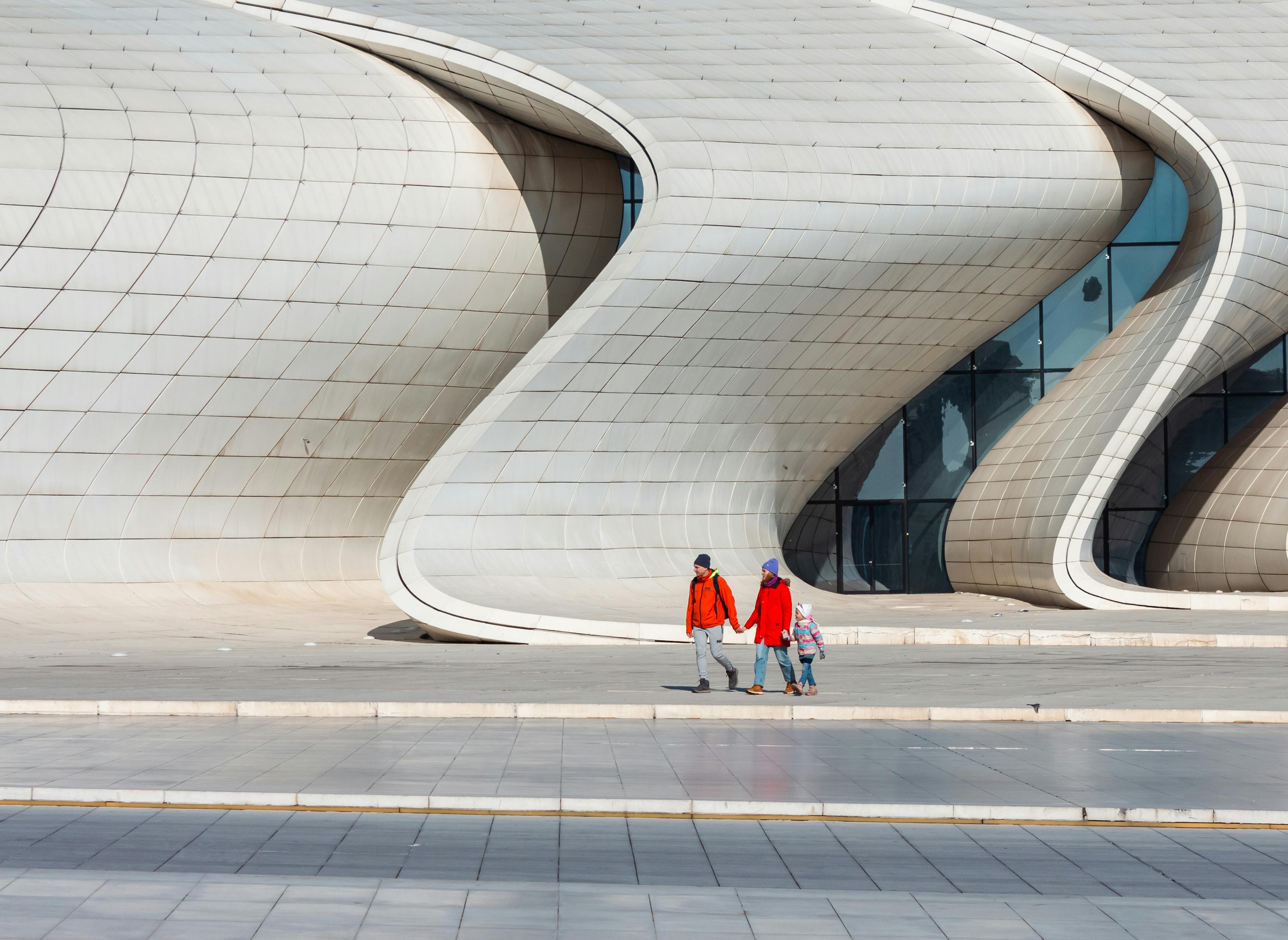 Family holding hands while walking by the modern facade of Heydar Aliyev Centre in Baku.