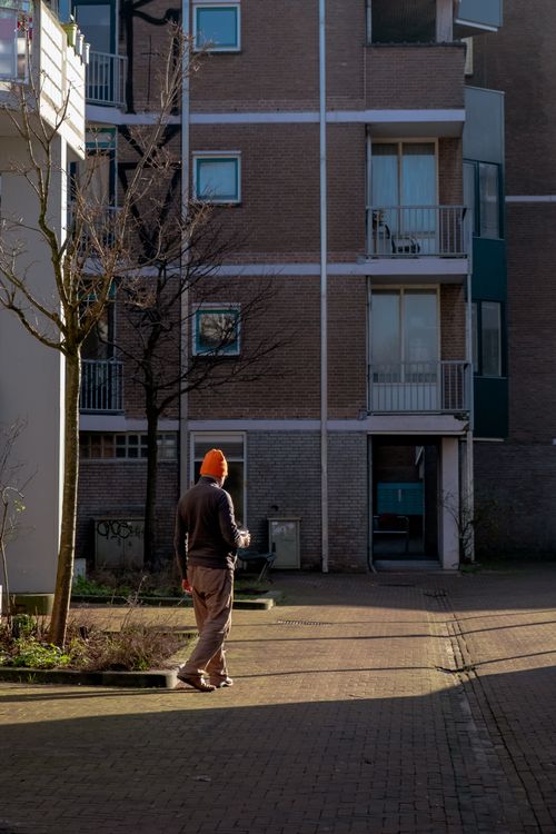 Free Man in orange beanie walks by residential building on sunny day. Stock Photo