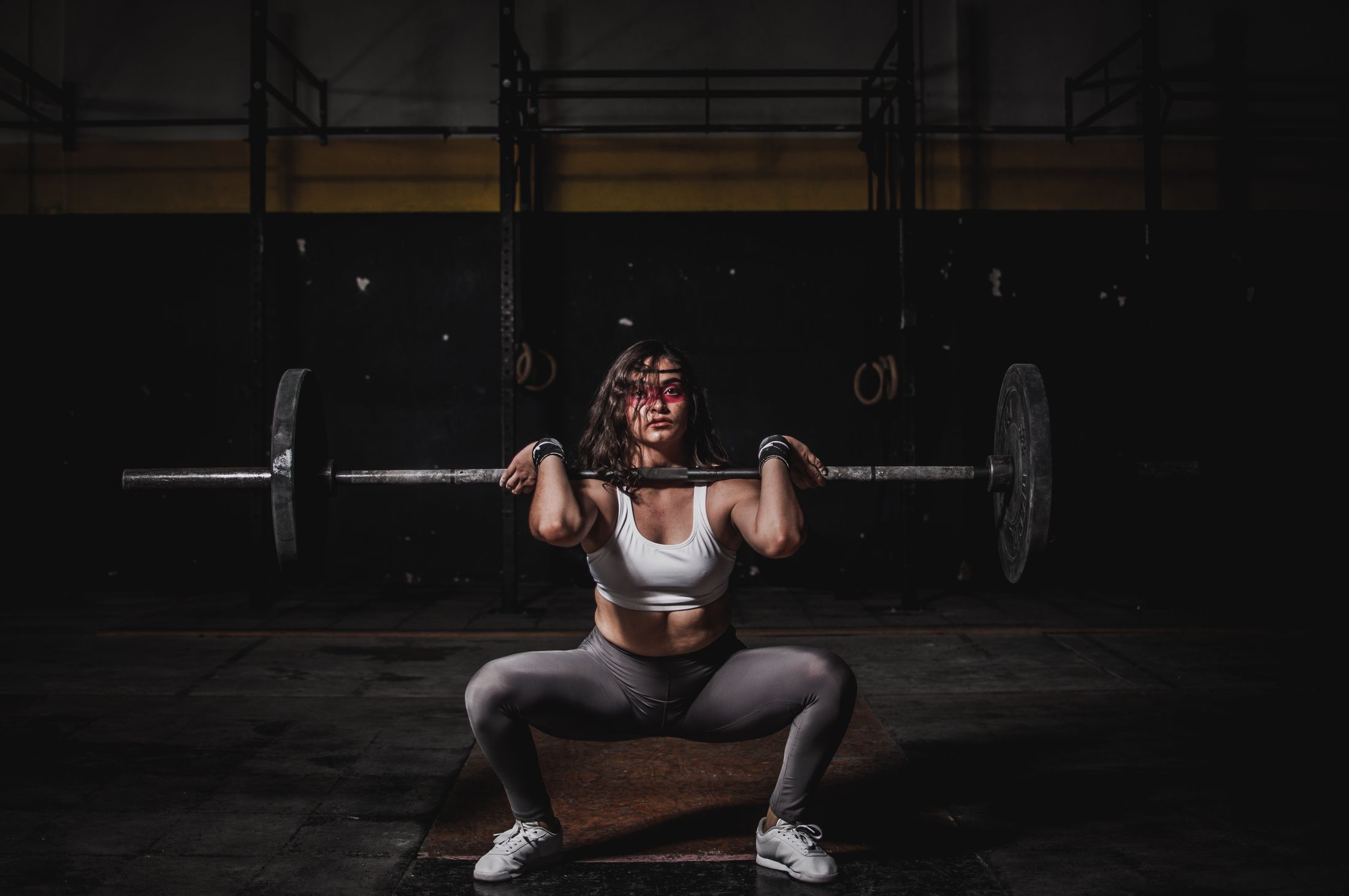 A lifter holds a barbell across her shoulders at the bottom of a front squat in a dark gym