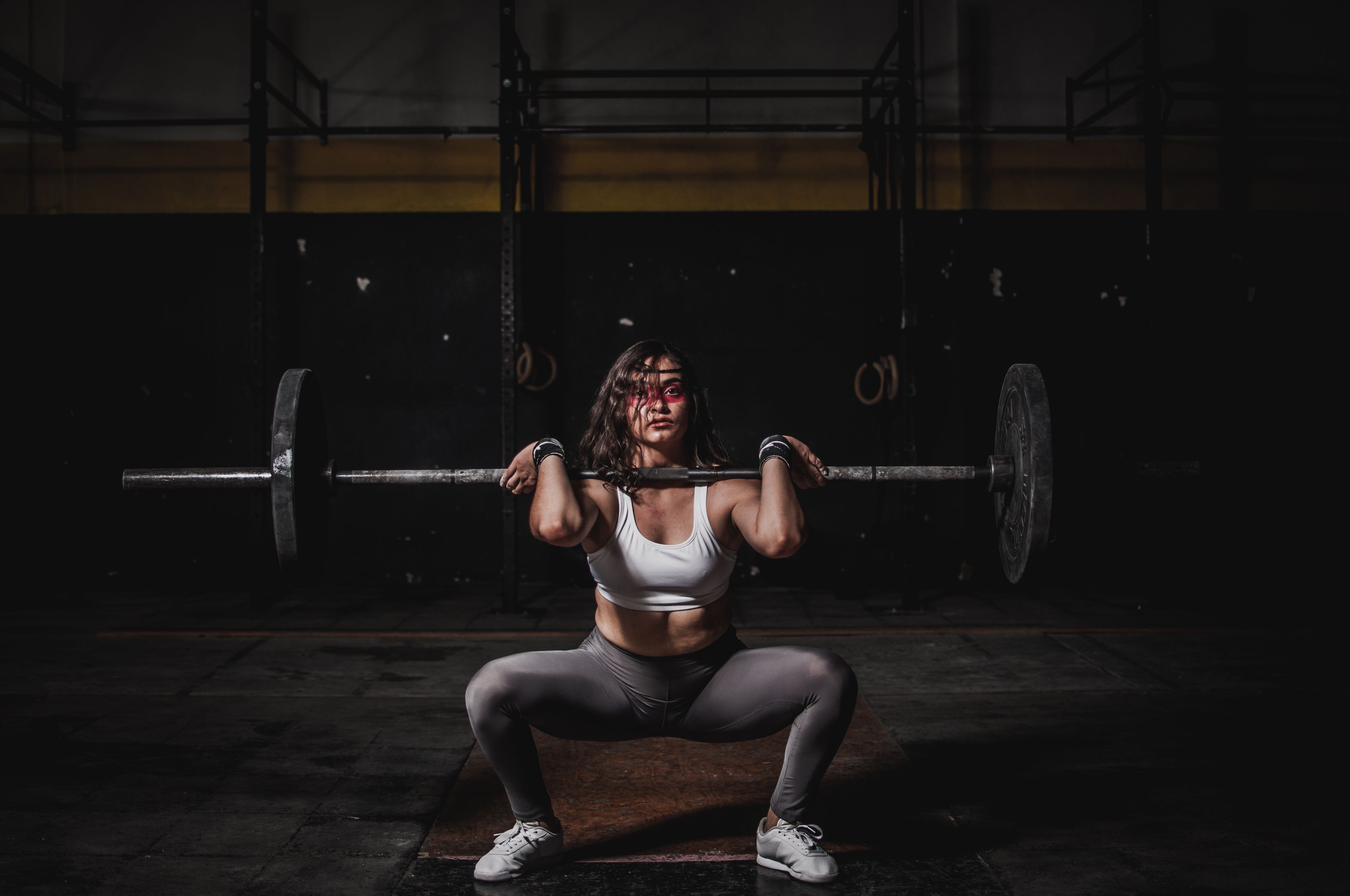 A strong female weightlifter squats with a barbell in a dimly lit gym, showcasing power and fitness.