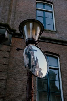 Street lamp with mirror reflecting a building facade in the cityscape.