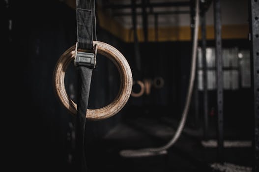 Close-up of a wooden gymnastic ring hanging in a dimly lit indoor gym, emphasizing fitness and training.