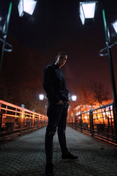 A young man stood on an illuminated bridge at night against the background of city lights.