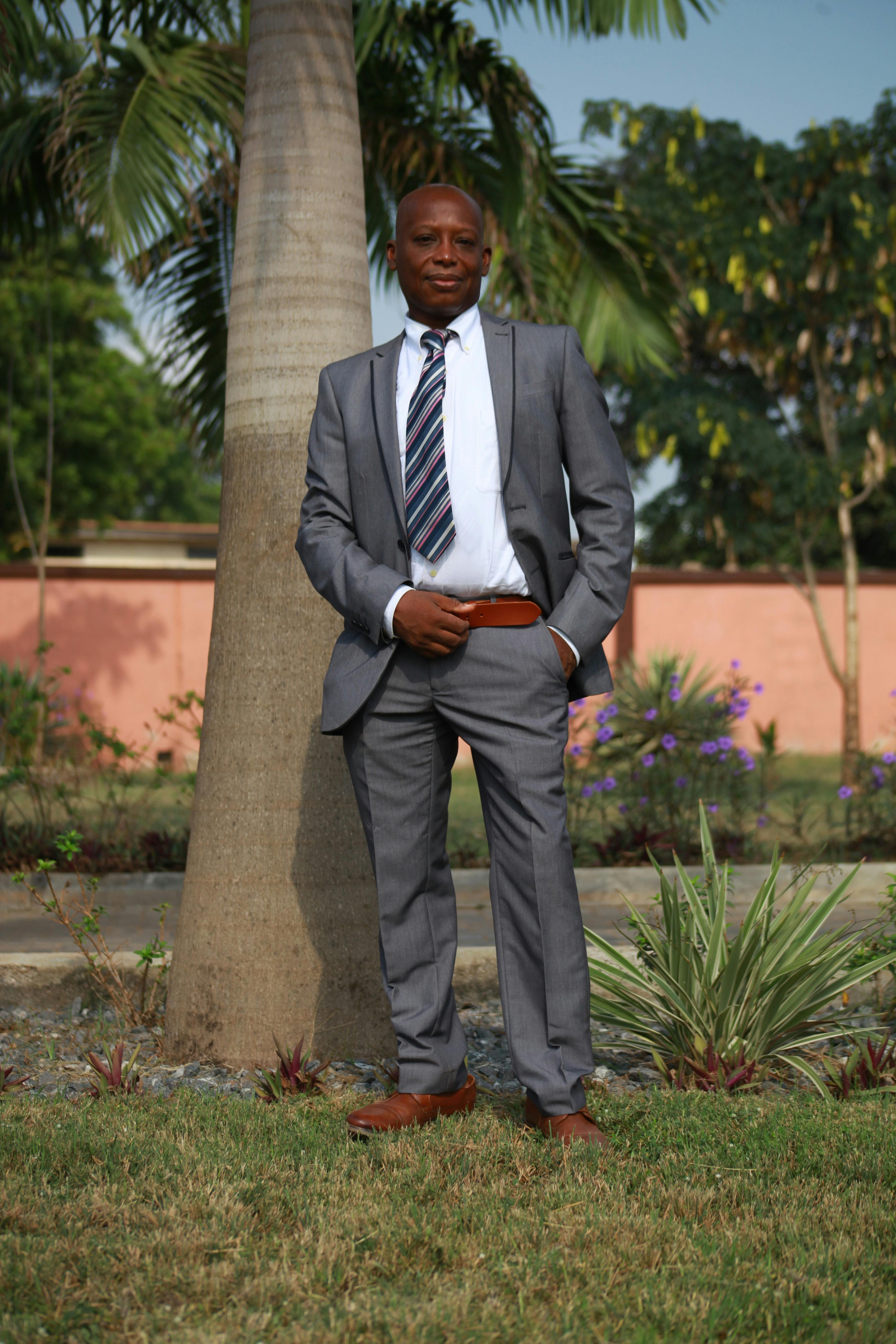 Confident man in a suit posing outdoors by a palm tree, showcasing elegance and style.