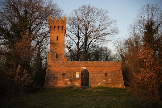 Majestic brick tower amidst fall foliage in Faenza, Italy, capturing the serene beauty of nature and history.