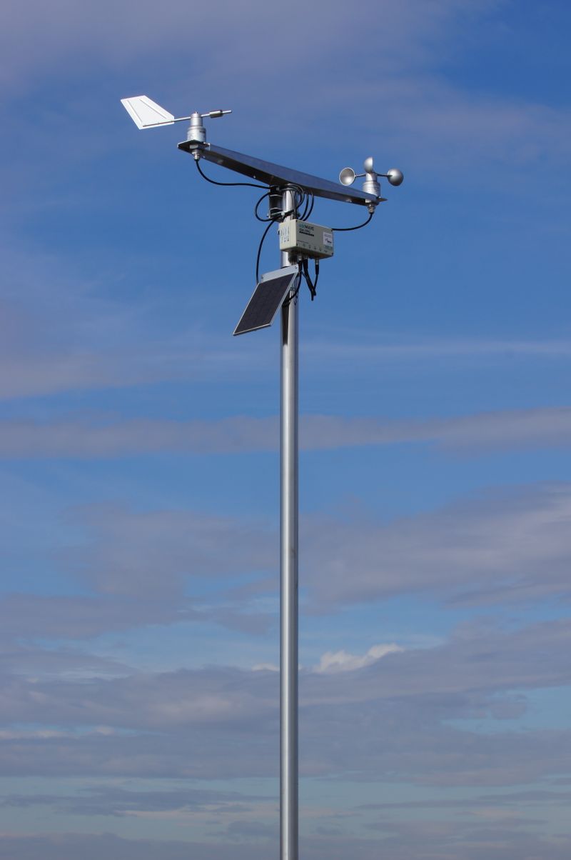 Solar-powered wireless weather sensor station mounted on a pole in a field, demonstrating outdoor IoT sensor deployment