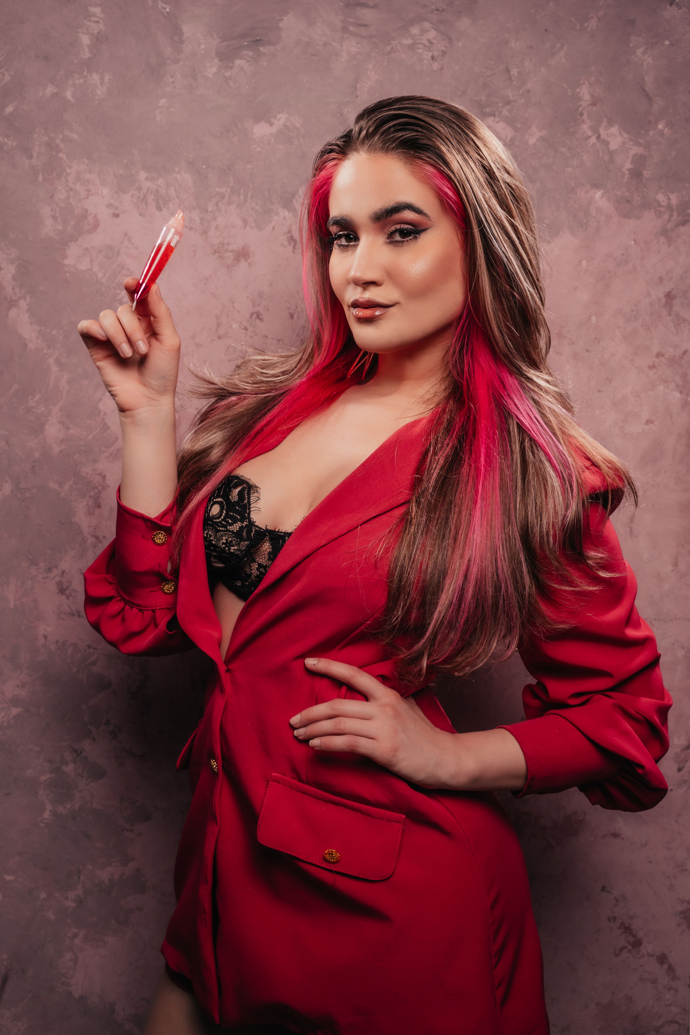 Fashionable woman in red blazer holding lipstick. Studio portrait with chic style.