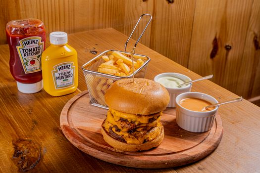 Tasty cheeseburger with fries and dips on a wooden table, perfect for fast food lovers.