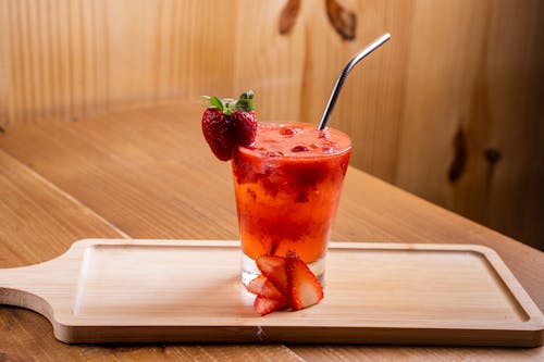 A strawberry drink on a wooden tray with a straw