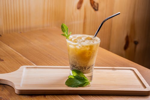 A drink with mint leaves and ice on a wooden tray