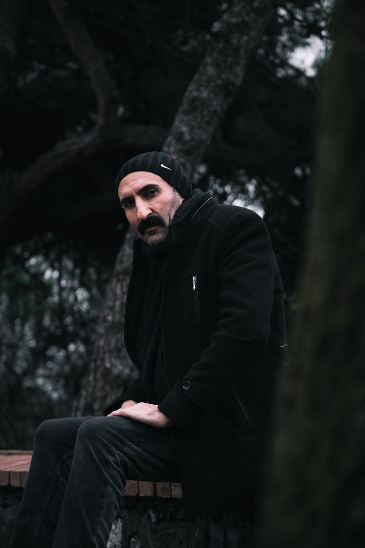 Man In Warm Clothing Sitting On A Bench Outside 