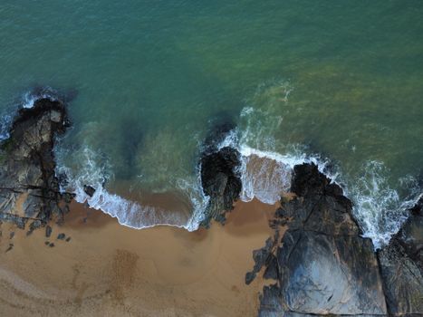 A stunning aerial view of a rocky beach in Brazil with waves crashing onto the shore.