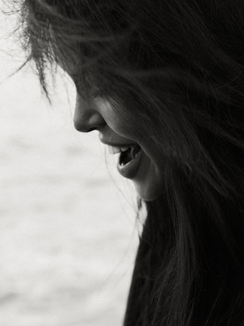 Side view black and white photo of a young woman laughing with long hair.
