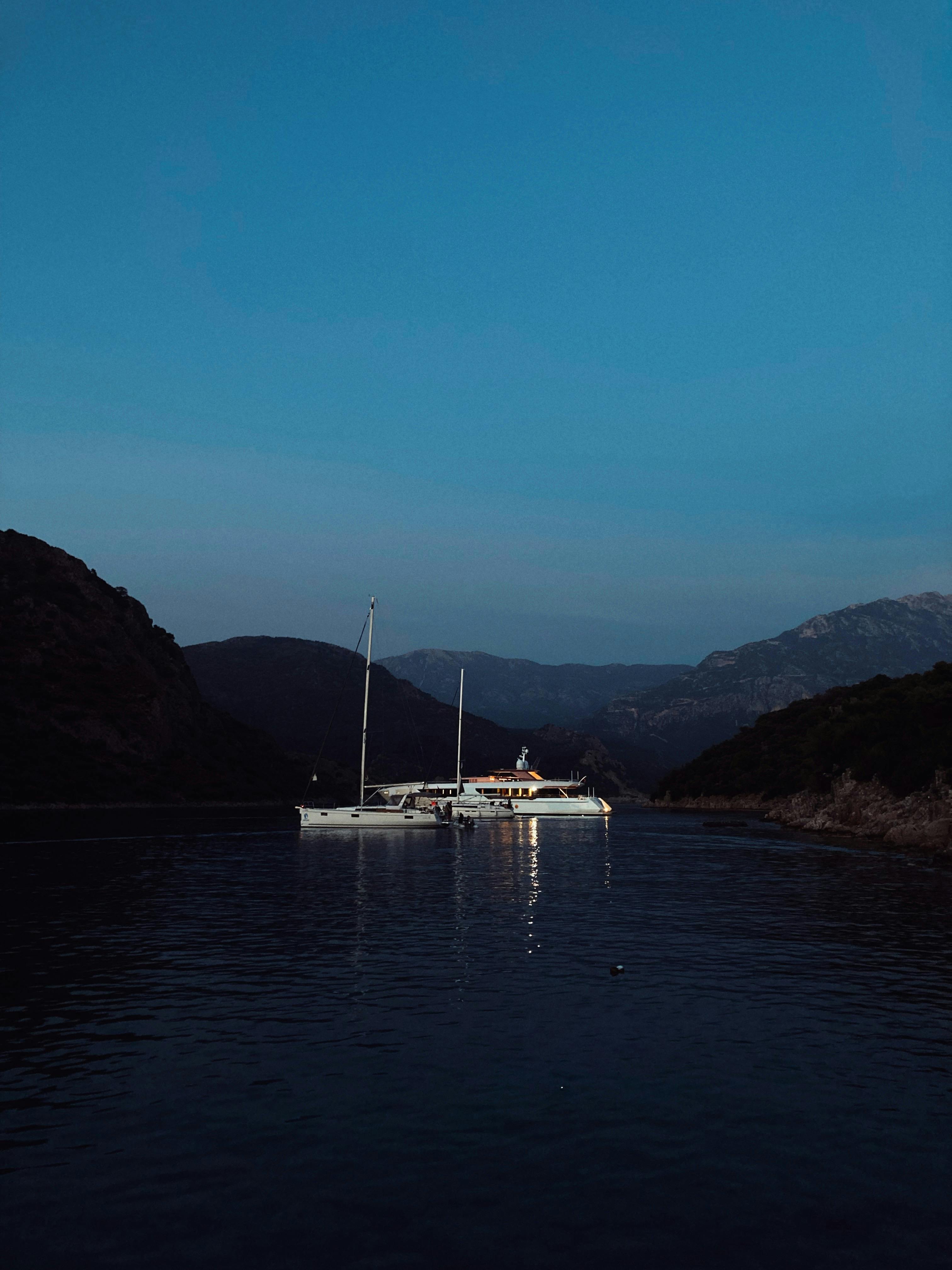 A tranquil sailboat illuminated during twilight in Ölüdeniz, Türkiye, surrounded by majestic mountains.