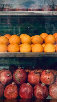 Vibrant display of fresh oranges and pomegranates in Rasht, Iran market window.