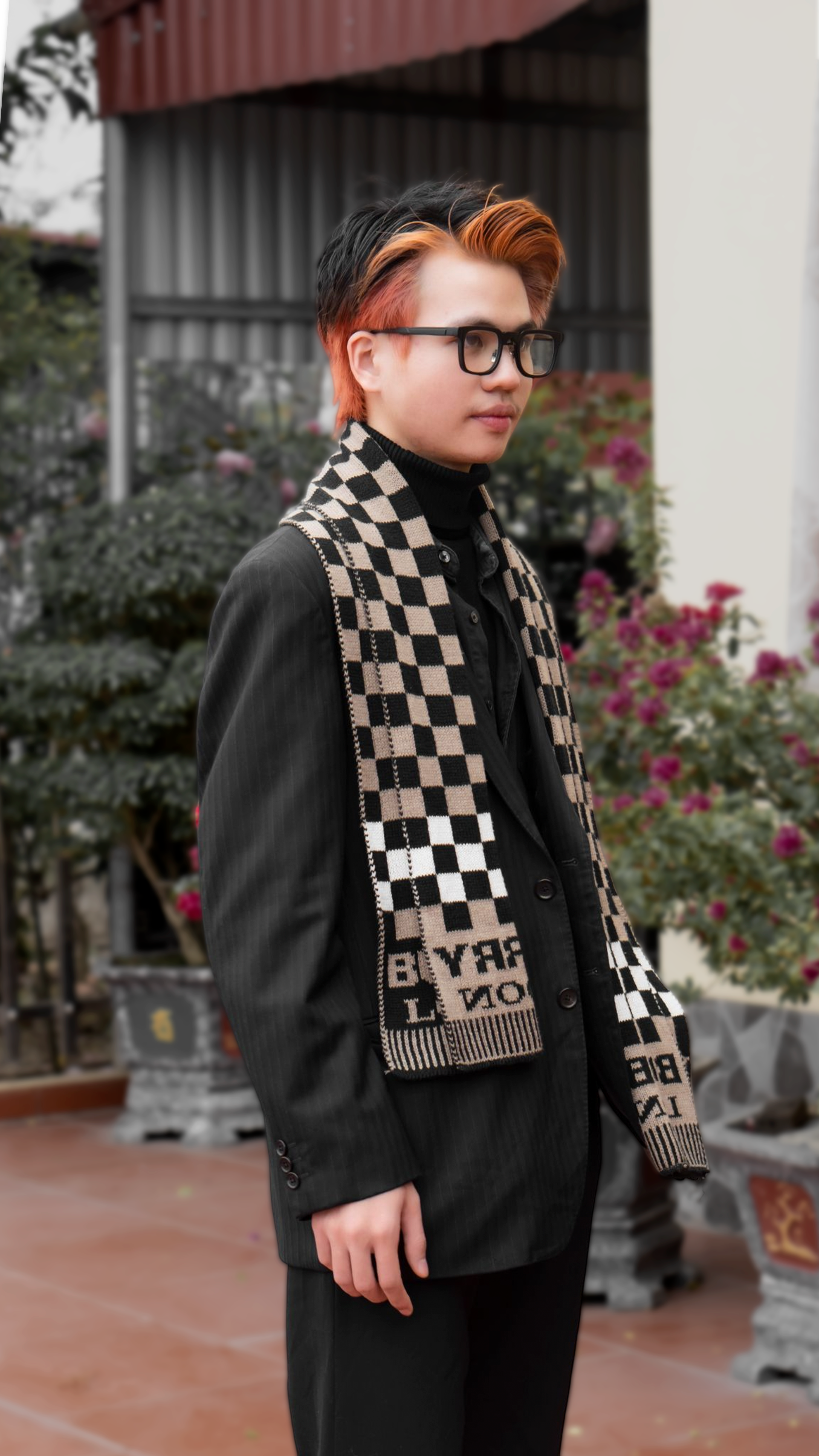 Asian man wearing eyeglasses and checked scarf, standing outdoors.