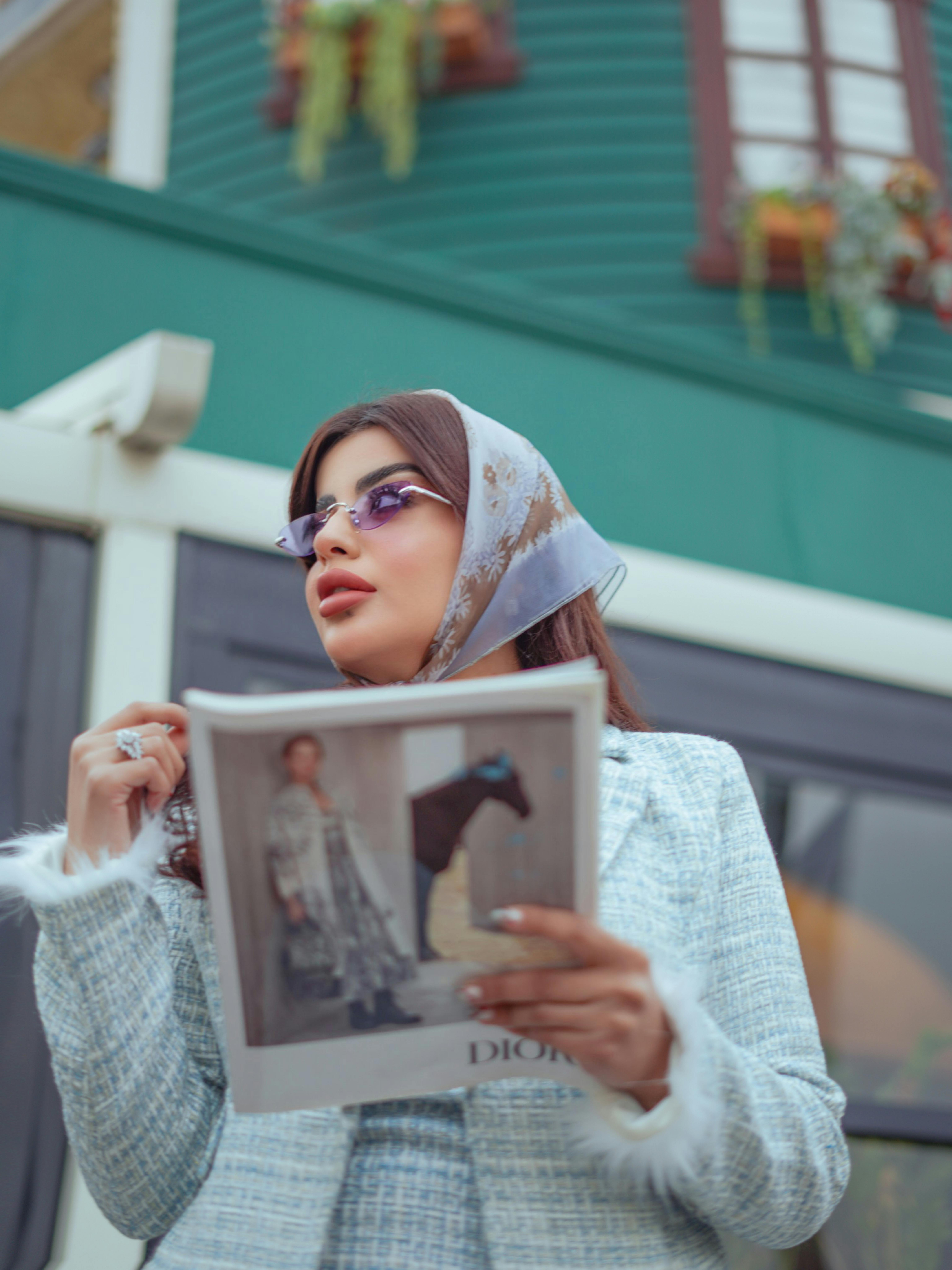 Fashionable woman holding a magazine outdoors in a stylish, urban scene.