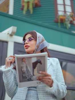 Fashionable woman holding a magazine outdoors in a stylish, urban scene.