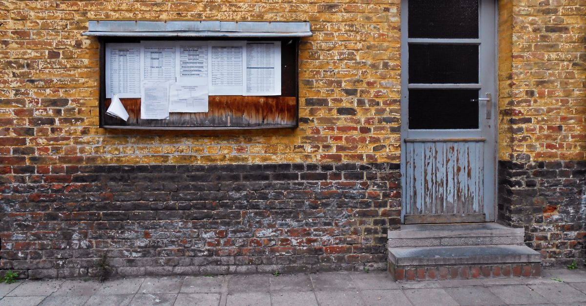 A rustic brick wall in Mons, Belgium, featuring a notice board and weathered door.