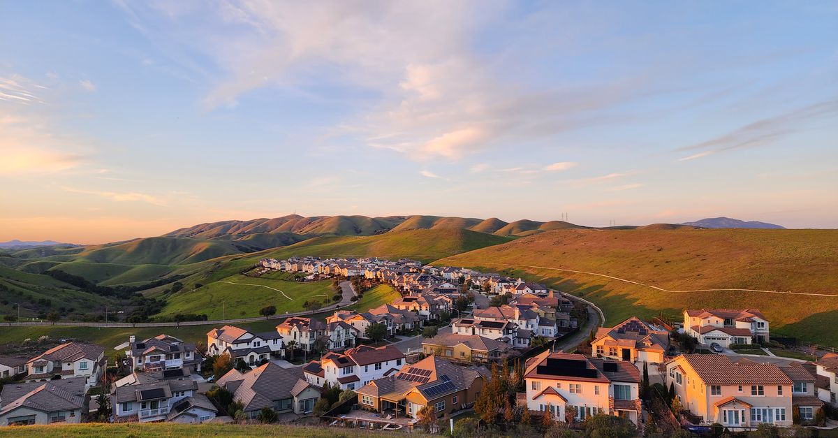 A picturesque suburban village surrounded by rolling hills under a clear summer sky.