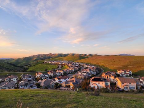 A picturesque suburban village surrounded by rolling hills under a clear summer sky.