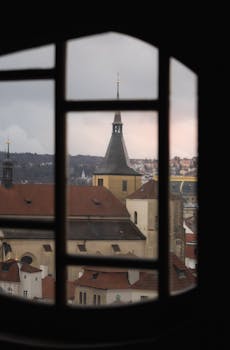 A picturesque view of a historic Prague building captured through a Gothic-style window.