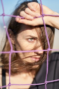 一位头发随风飘扬的女人透过户外的网窥视的艺术肖像