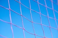 粉红色排球网图案与清澈蓝天的特写，展现了几何形状之美