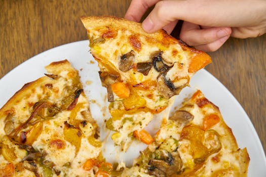 Close-up of a hand picking a slice of vegetarian pizza with mushrooms and cheese.
