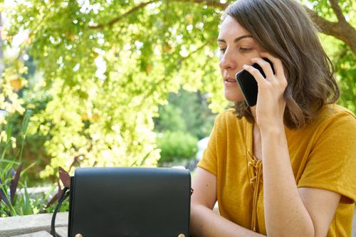 Free A woman in a yellow shirt makes a phone call outdoors amid lush greenery. Stock Photo