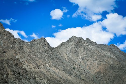 Free A stunning view of a rocky mountain range beneath a vibrant blue sky with scattered clouds. Stock Photo