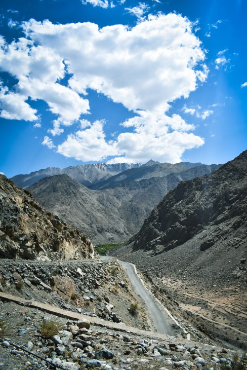 Free Discover a winding road through rugged mountains under a striking blue sky with fluffy clouds. Stock Photo
