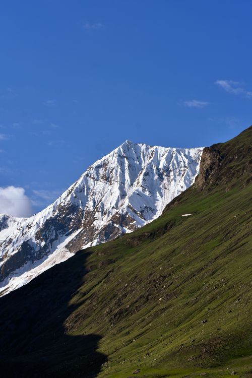 Free Majestic snowy mountain peak with lush green slopes under a clear blue sky, ideal for nature enthusiasts. Stock Photo