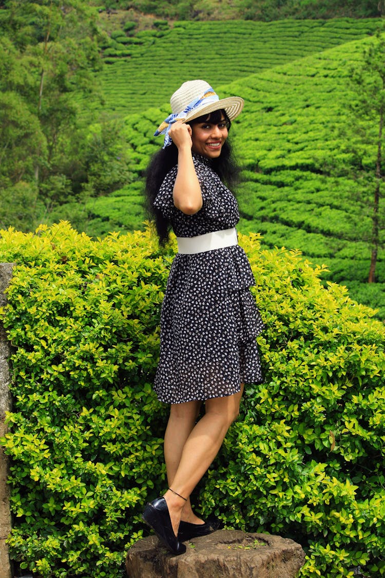 Woman In Dress Posing Near Bush And Green Plants