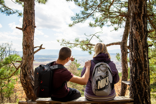 A boy shows a woman something in the distance. Together in the forest they sat on a bench. Rest in nature.