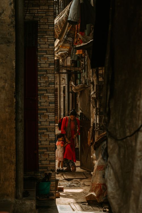 Free A warm, candid moment as a mother and child walk through a narrow urban alley filled with character. Stock Photo