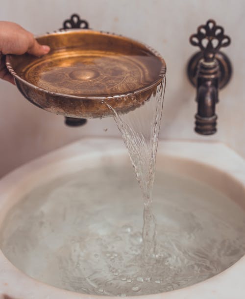 Pouring Water from Golden Bowl into Washbasin