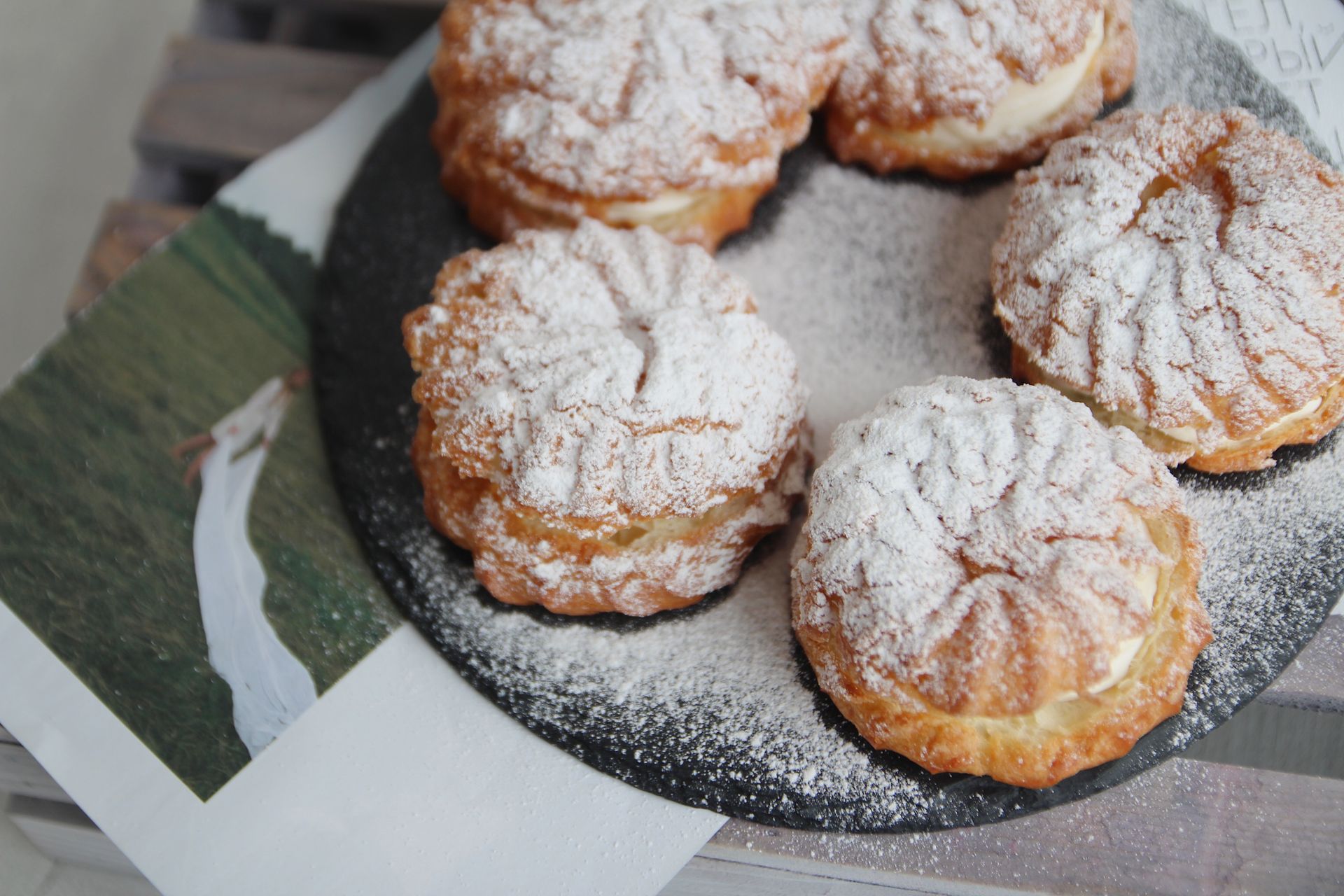 Delicious classic French cream puffs dusted with sugar, presented on a rustic slate tray.