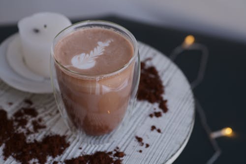 Photo of a Glass Mug of Coffee with a Candle in the Background