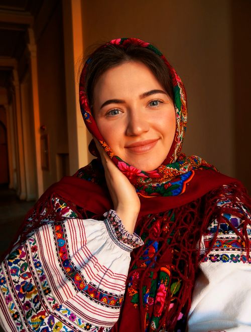 Free Portrait of a young woman wearing vibrant traditional Slavic attire and a colorful headscarf indoors. Stock Photo