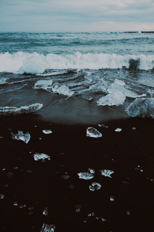 Free Captivating view of Iceland's black sand beach with ice formations and crashing waves. Stock Photo