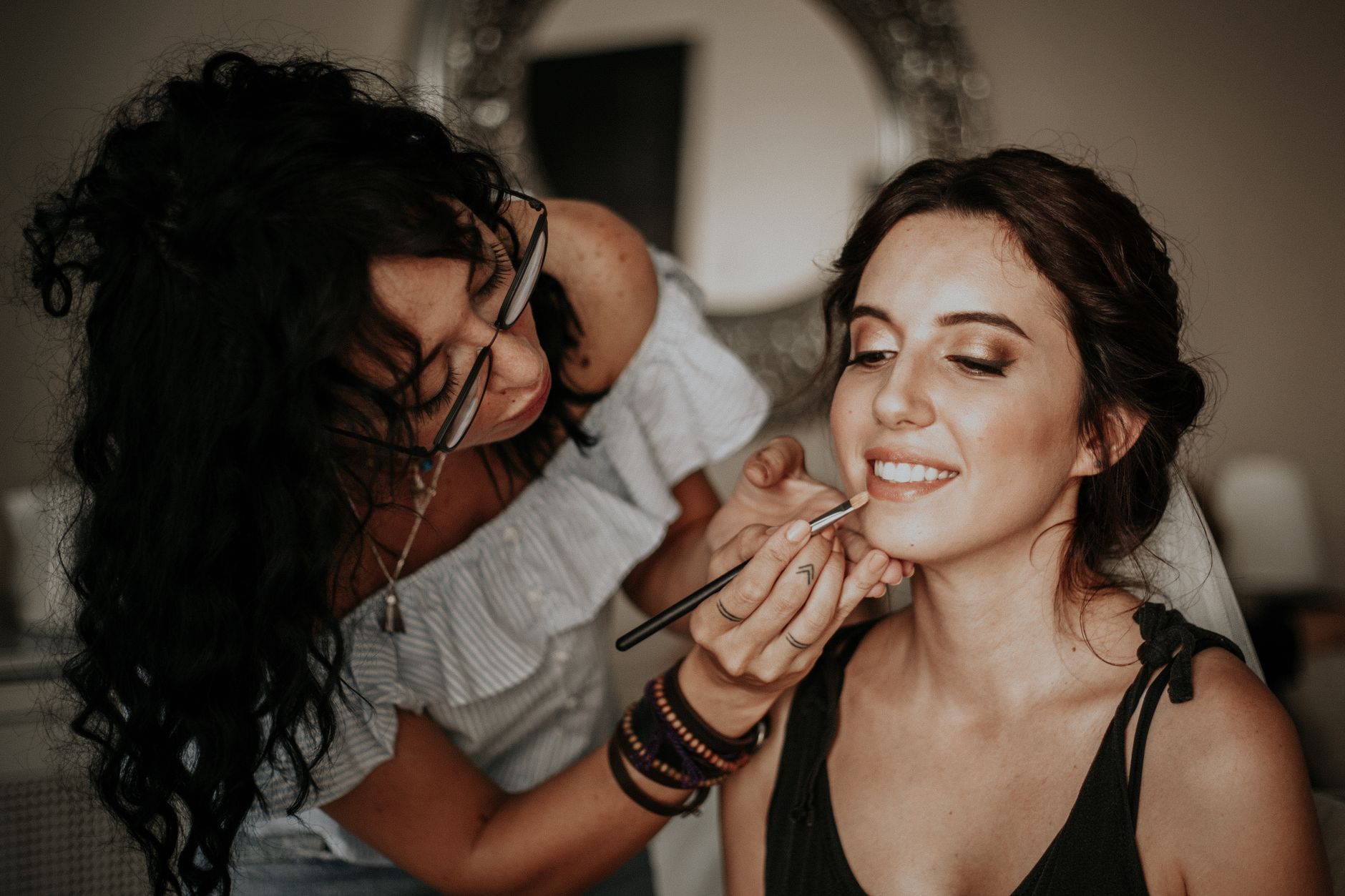A makeup artist skillfully applies lipstick to a smiling woman in an indoor setting.