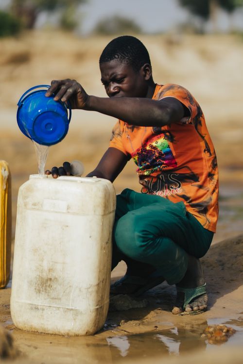 Free African man pouring water into a canister on a sunny day in Cape Town, South Africa. Stock Photo