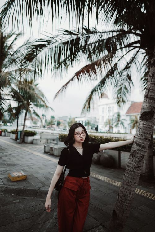 Free Stylish young woman posing under palm trees in a vibrant urban setting. Stock Photo