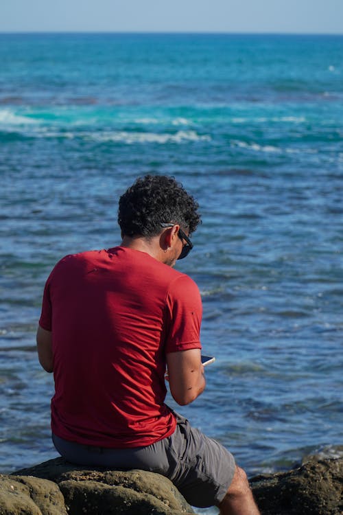 Man Sitting on Rocks near Sea