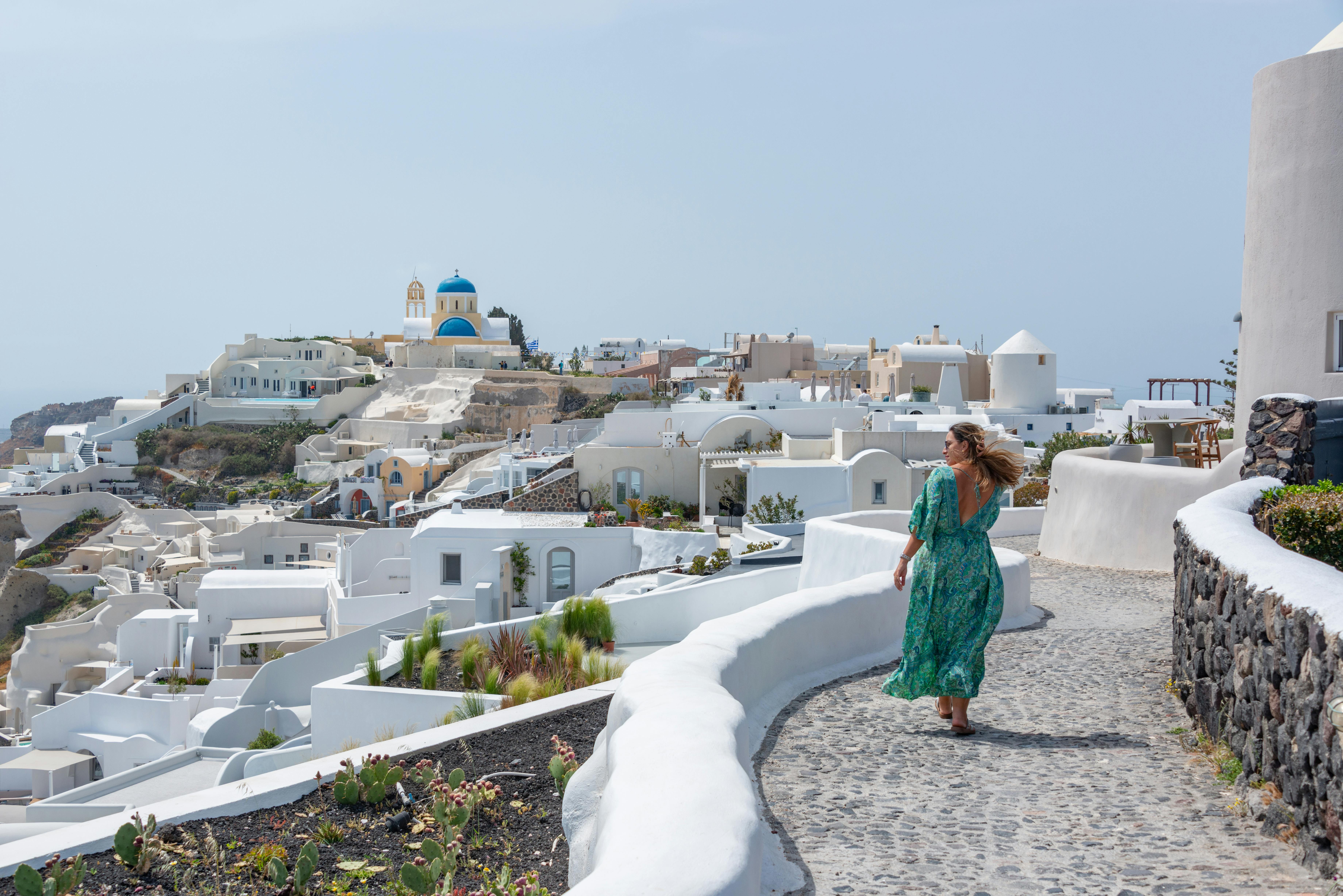 A woman walks through the picturesque, whitewashed streets of Santorini on a sunny day.