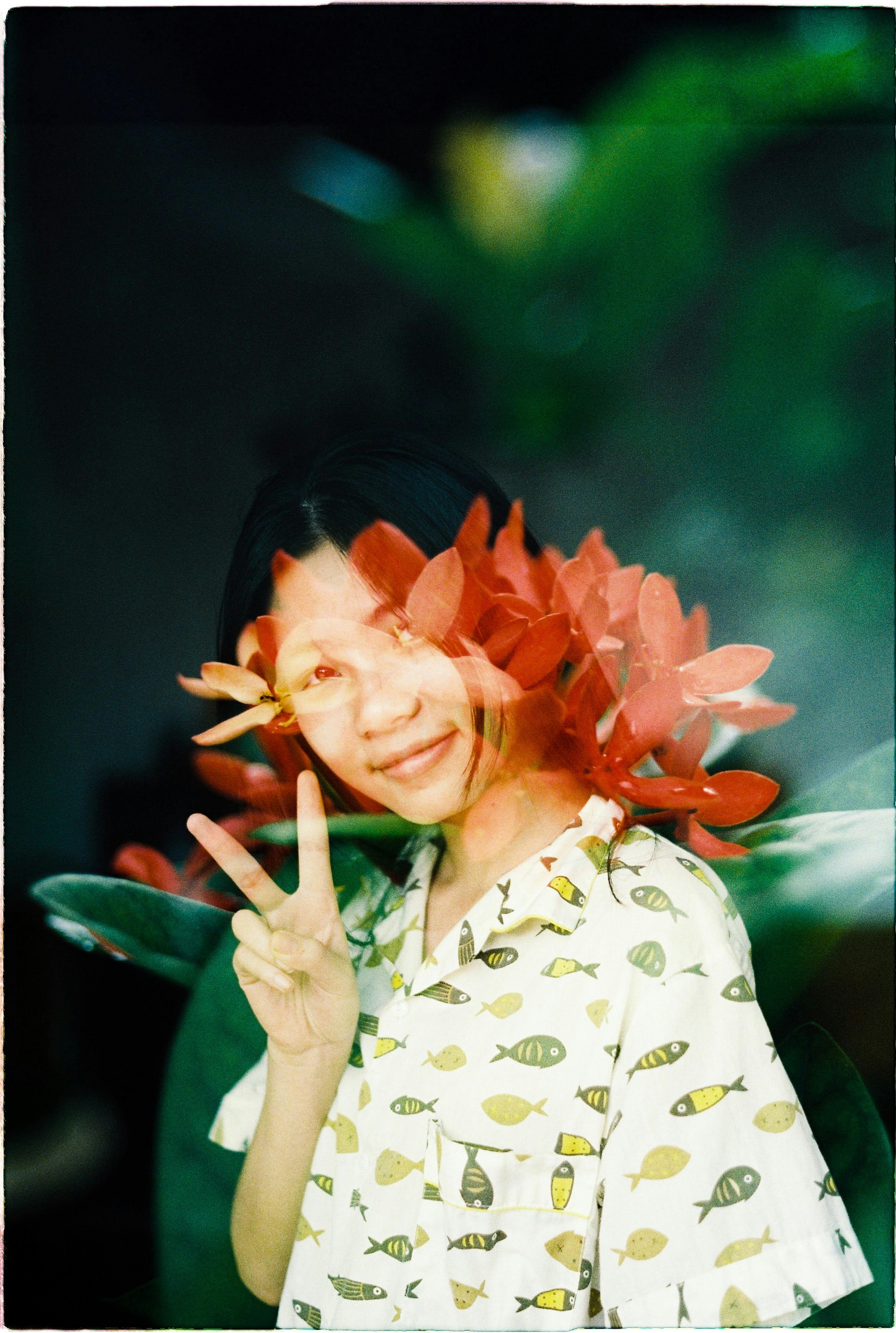 Artistic double exposure of a woman showing a peace sign with floral overlay.